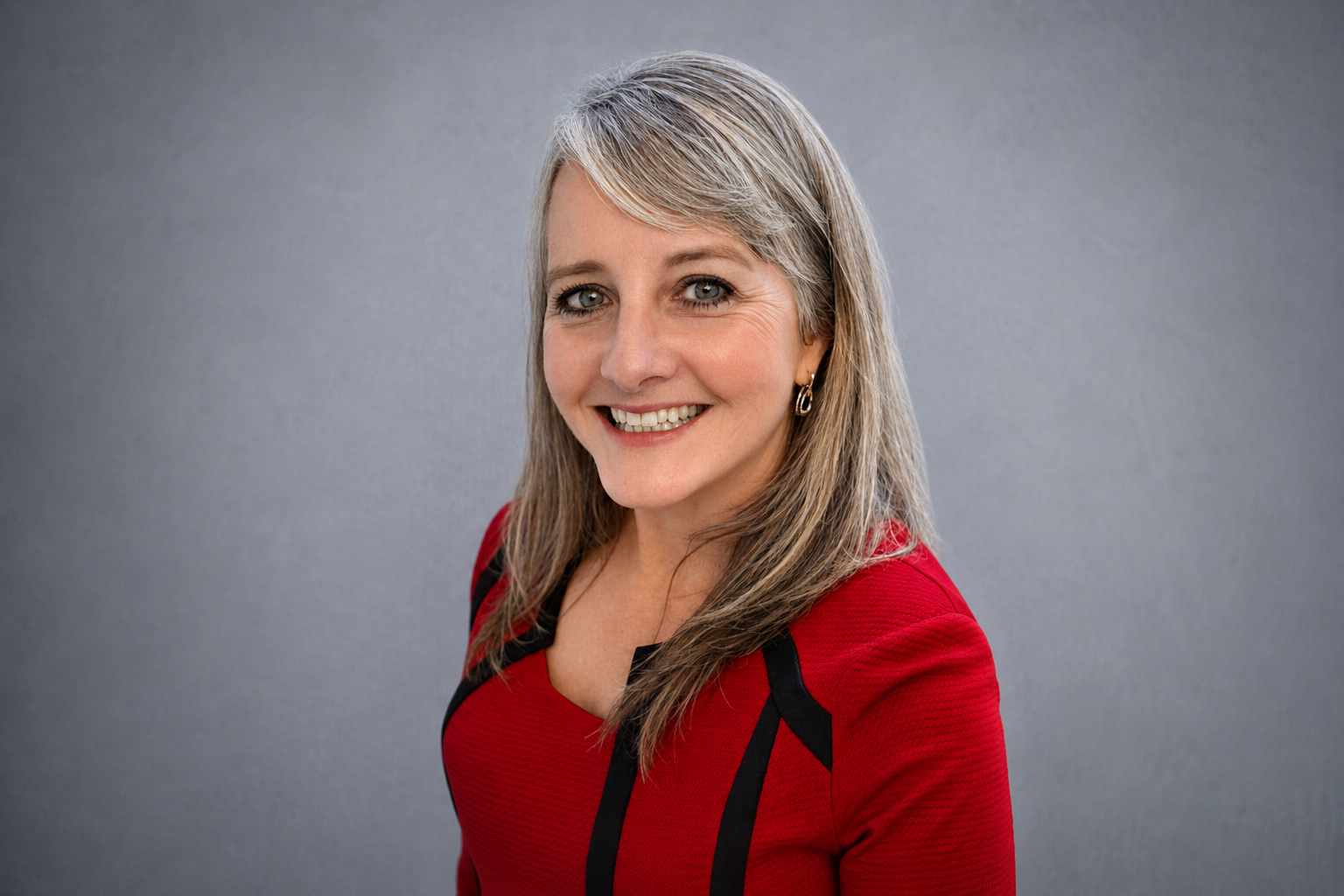 A professional headshot of a woman in a red suit.